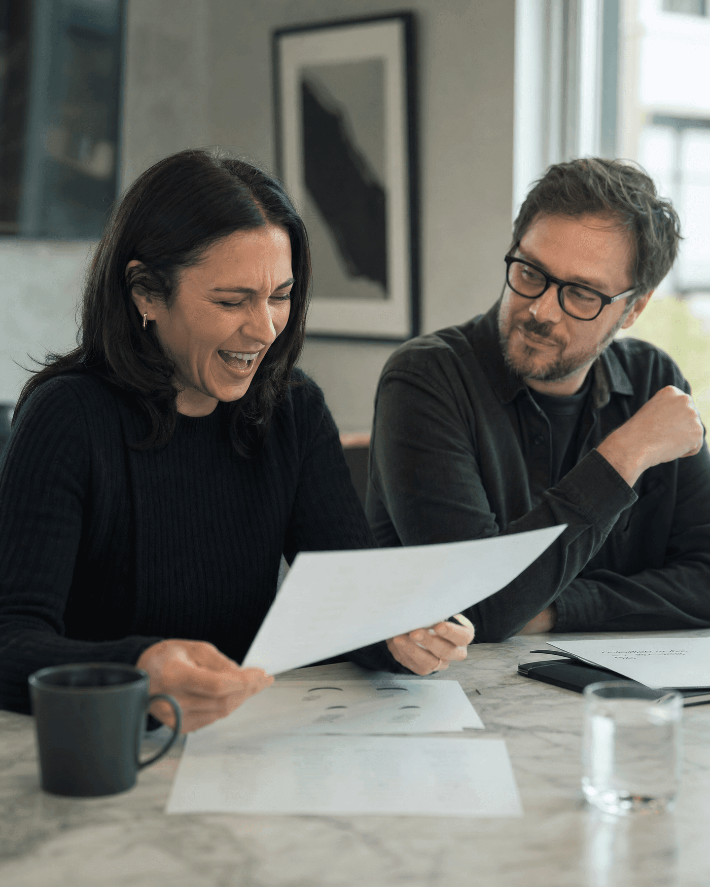 Two native-speaker reviewers reading a name shortlist aloud, one mid-laugh at a name that landed wrong
