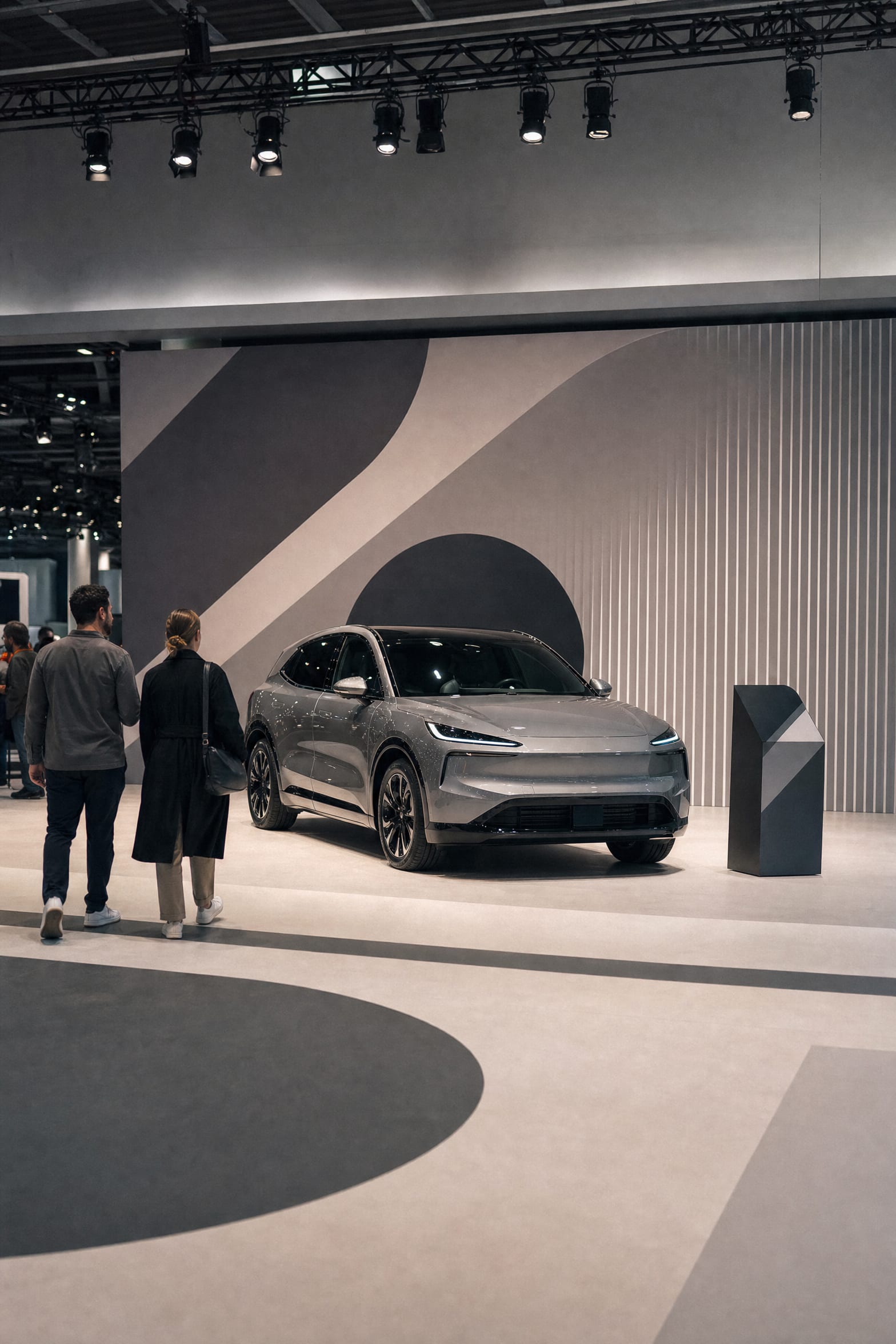 A premium electric vehicle on an international auto-show stand, one visual identity applied across the wall, the floor graphic, and a spec lectern, with visitors at human scale.