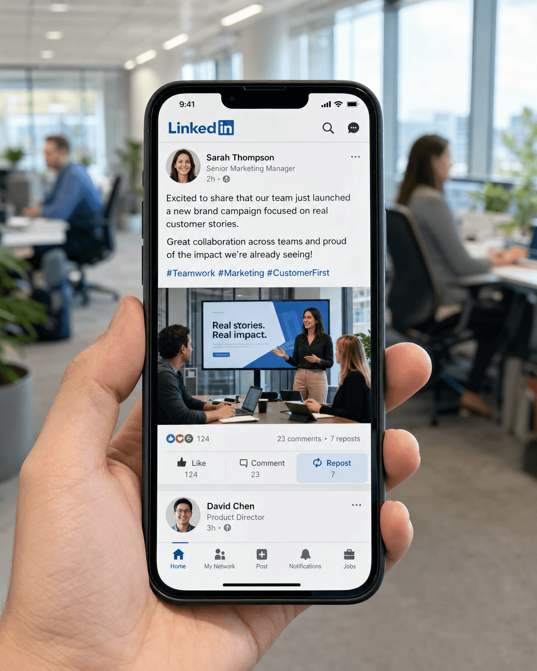 A hand holding a phone showing a LinkedIn feed post from an employee, with reaction, comment and repost counts