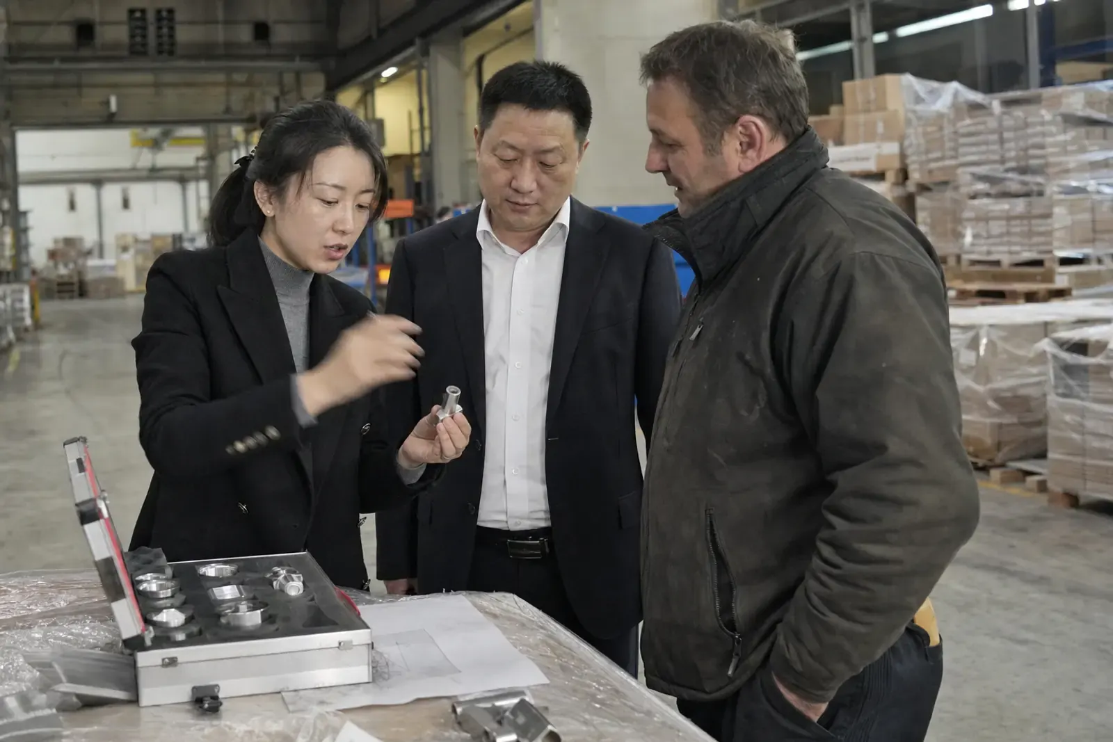 Two Chinese export managers showing a product sample to a European distributor on the floor of his warehouse