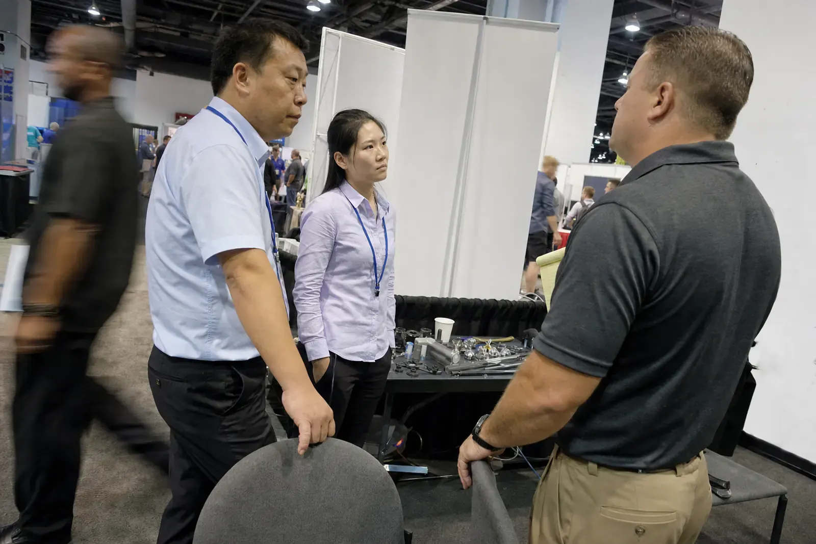 Two Chinese exporters at their booth on a busy American trade show floor, talking with a manufacturers representative