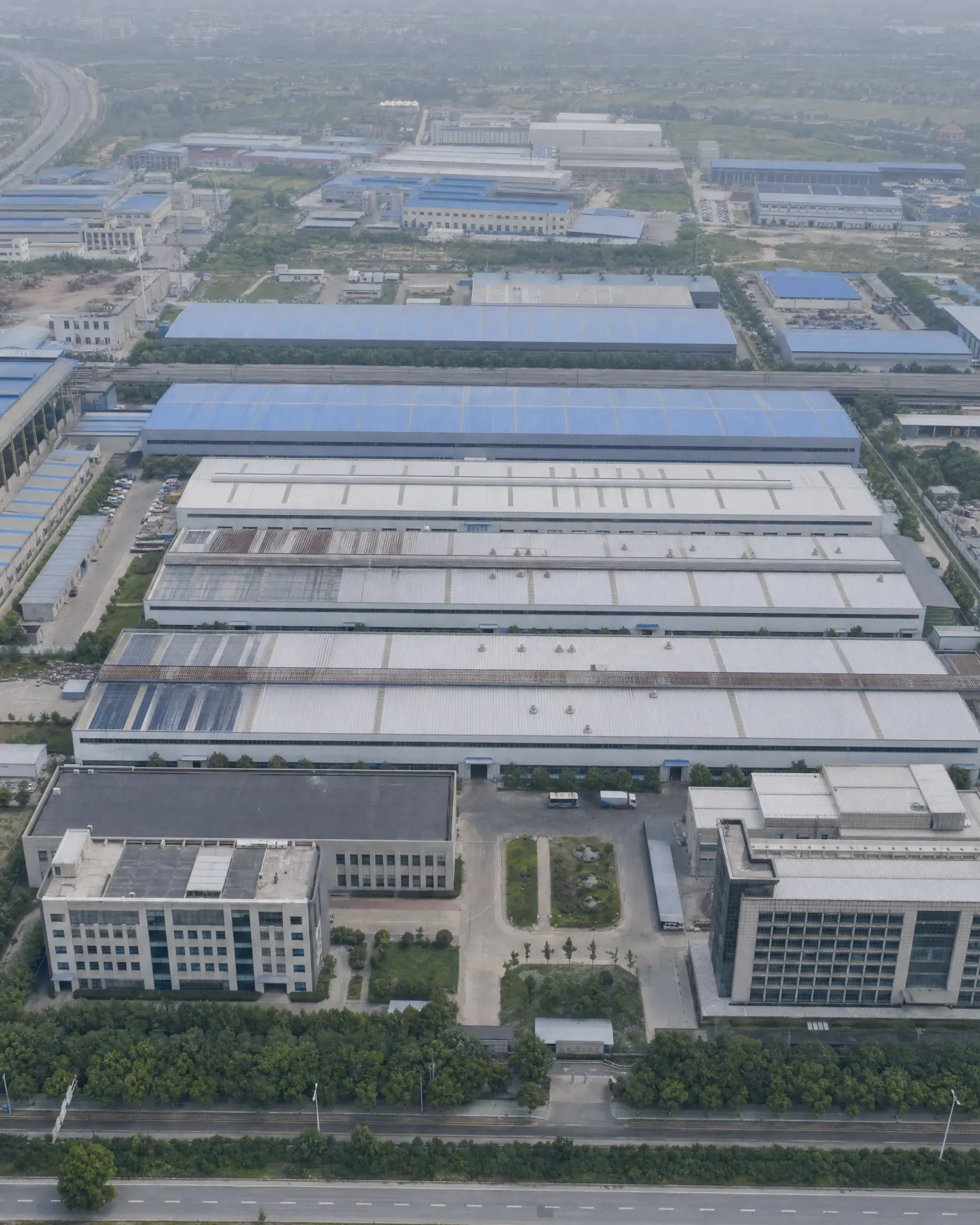 A flat, hazy aerial drone shot of a generic factory complex with no people