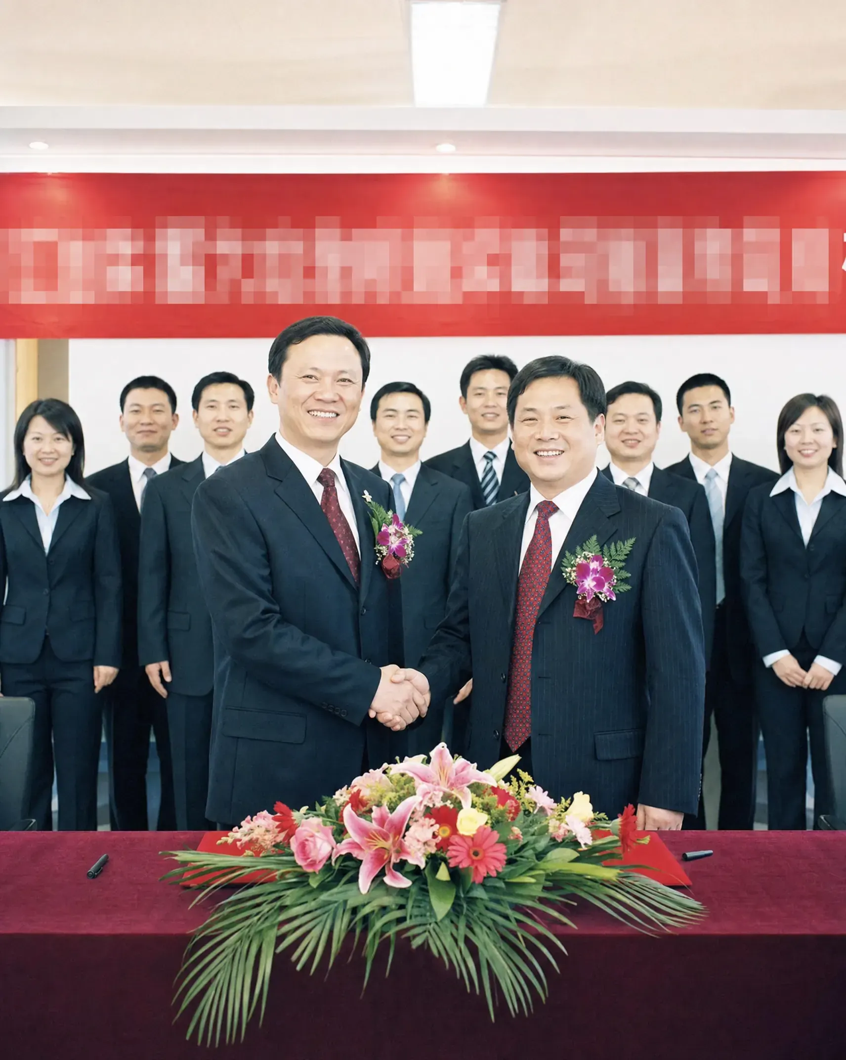 A posed corporate handshake under a banner with staff lined up facing the camera