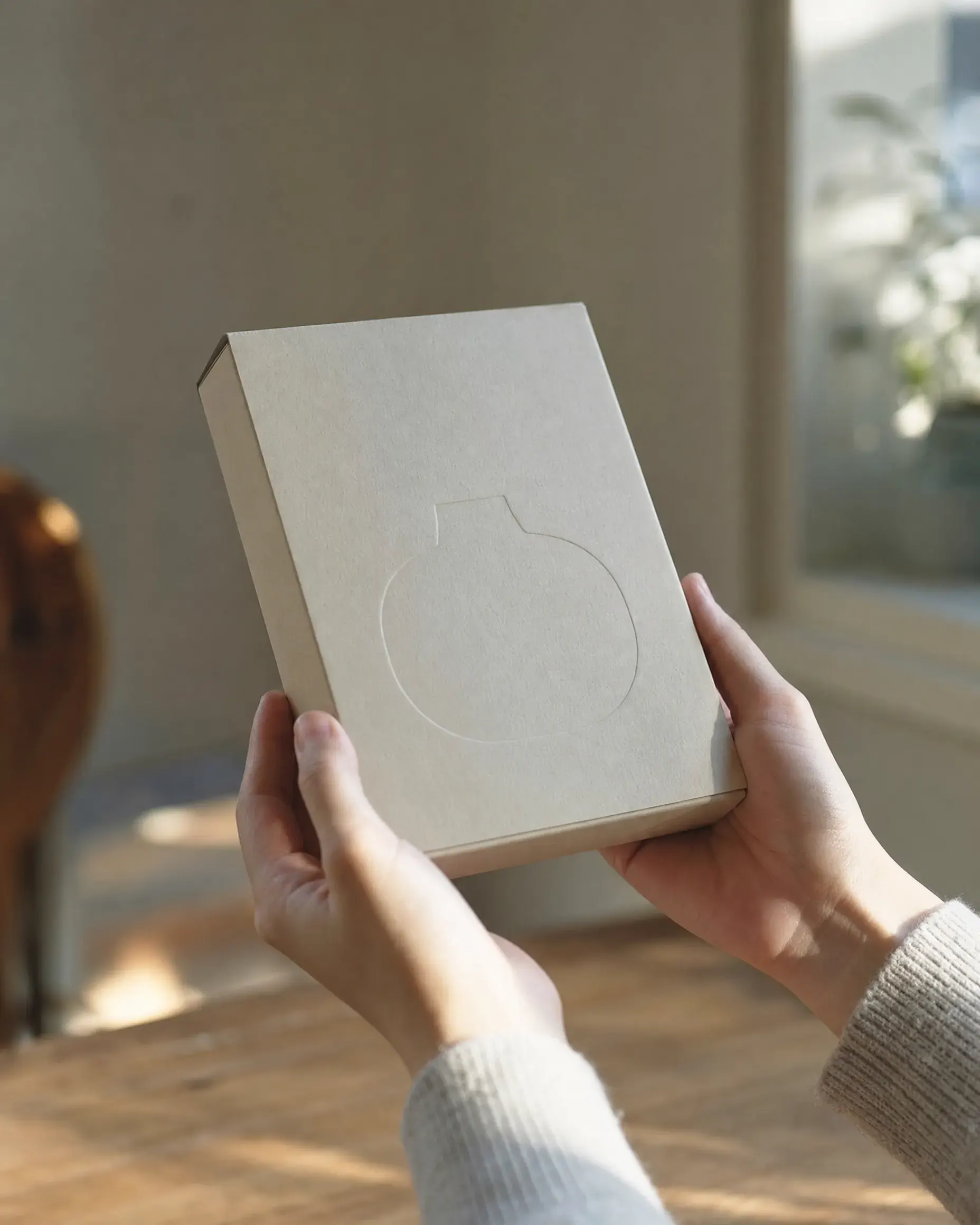 A finished product package held in two hands, turned to catch window light