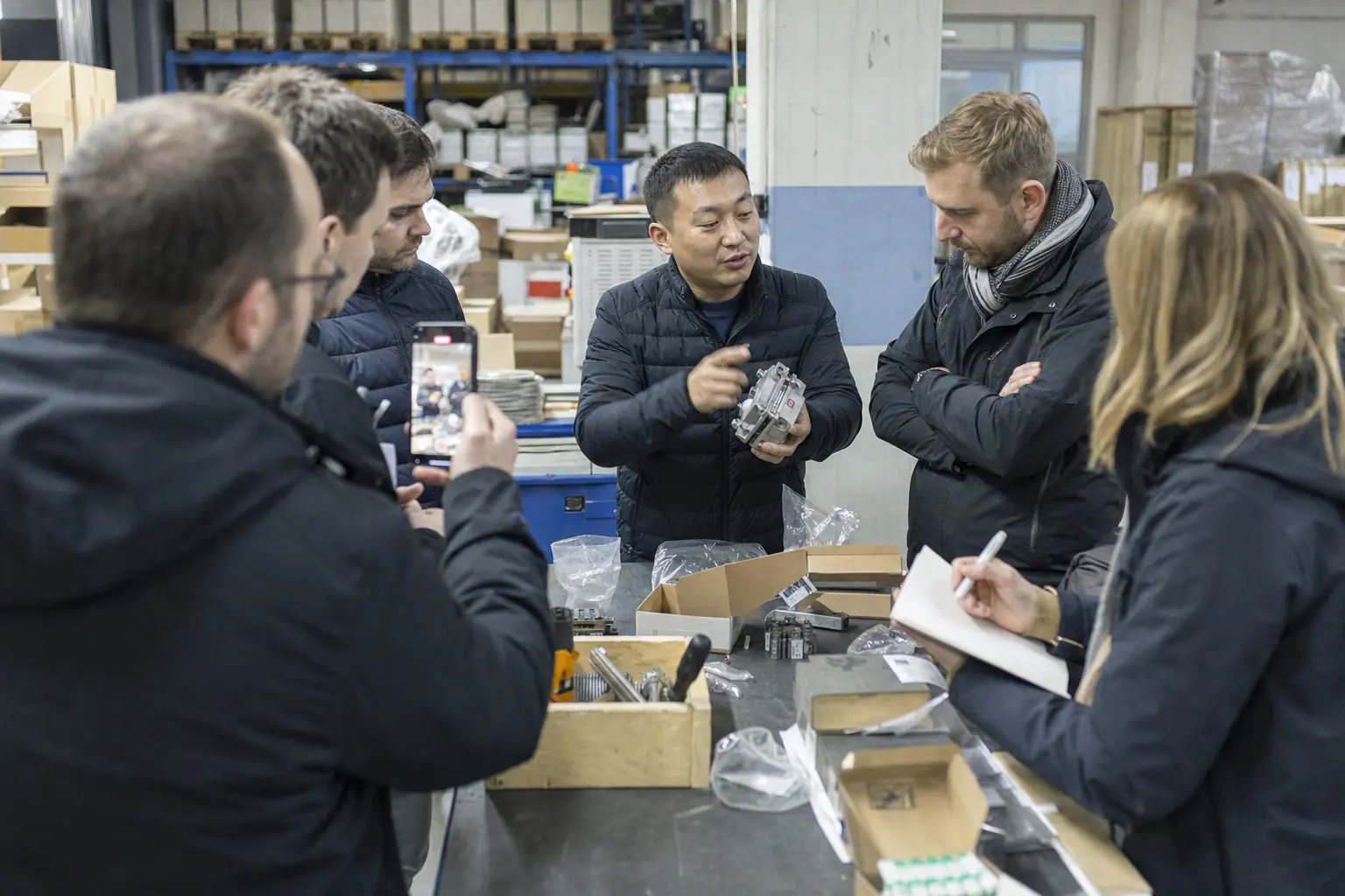 A Chinese product engineer training a European distributor’s sales staff around a warehouse workbench