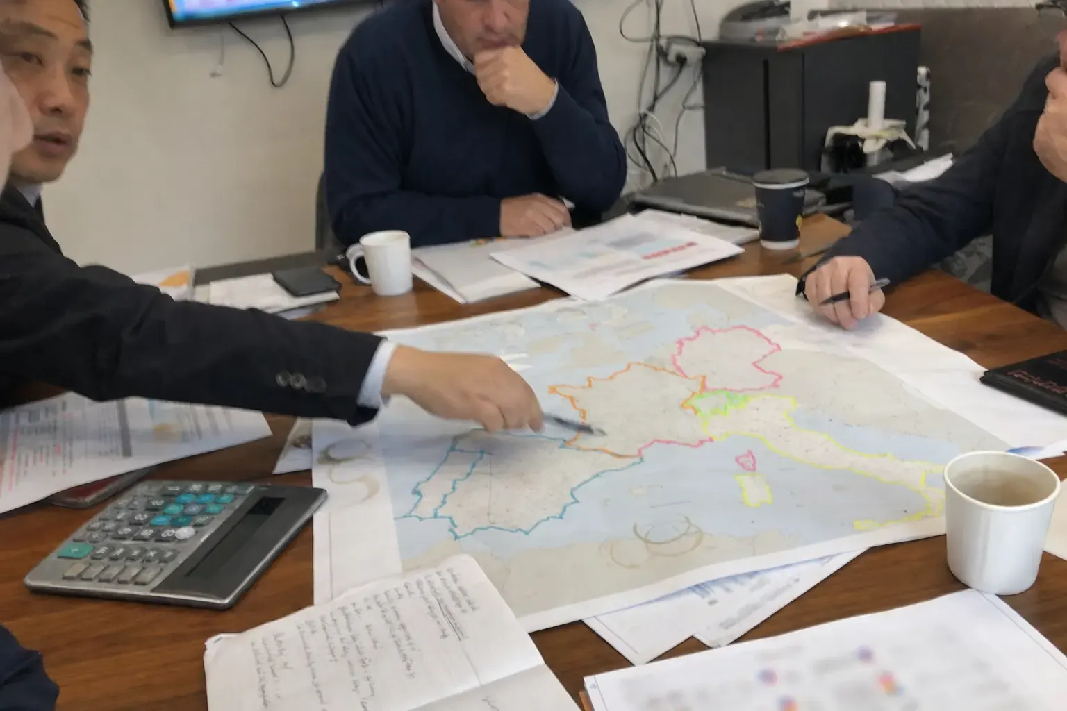 A Chinese export manager and overseas partners marking distributor territories on a printed map of Europe